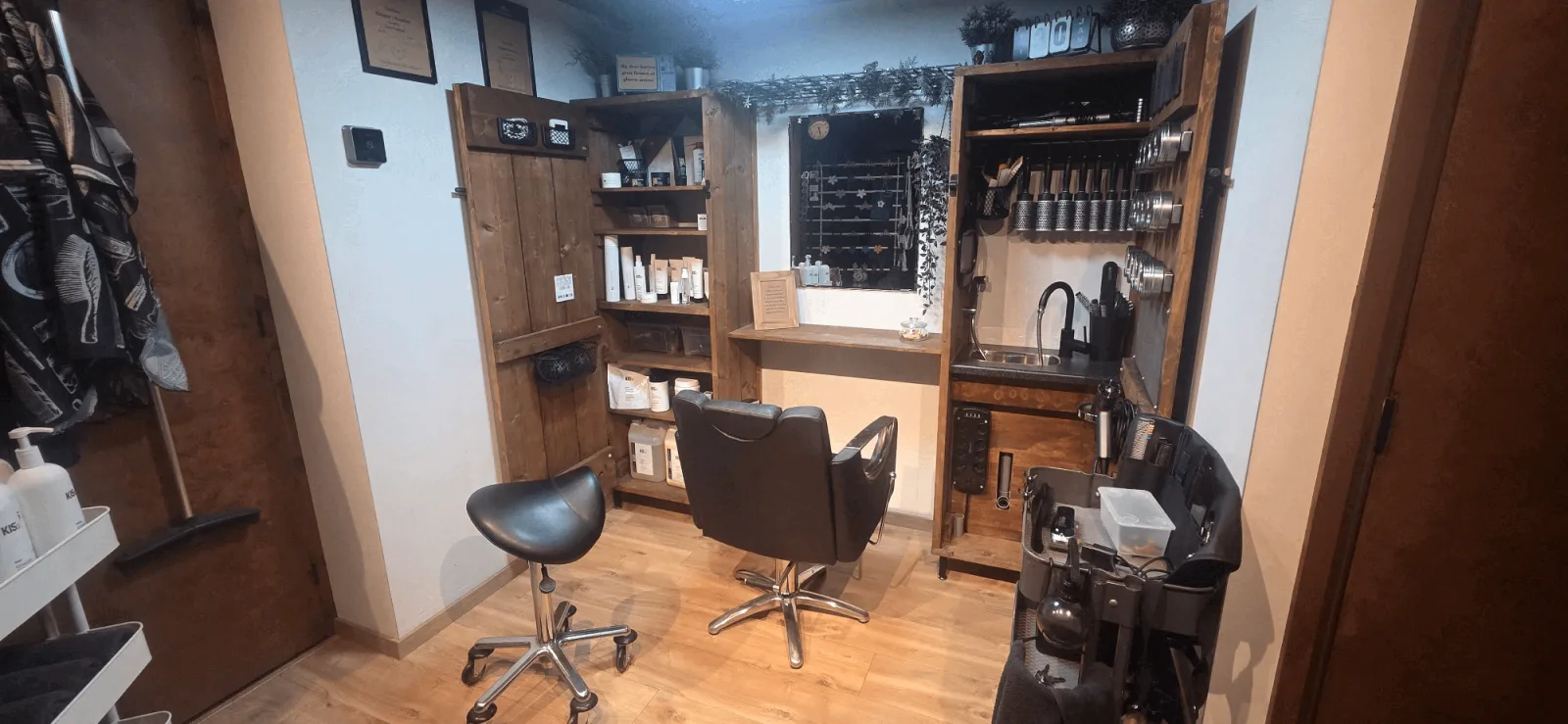 De salon van binnen: één stoel bij de wastafel, met kasten van steigerhout vol haarproducten.